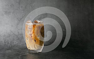 Iced latte coffee into a transparent glass with ice on black background studio photo.