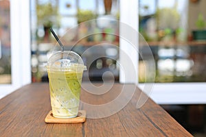 Iced matcha green tea latte with milk with brown straw in take away cup on wooden table at cafe