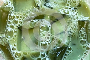 Iced matcha latte close up, texture of refreshing tea with transparent ice cubes and bubbles