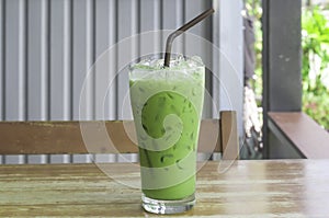 Iced matcha latte or condensed milk-added green tea in transparent glass with black straw on wooden table served at coffee shop