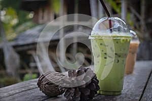 Iced milk green tea drink with dried pine cones on wooden table against old wood house background