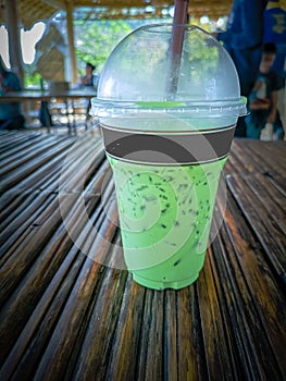 Iced milk green tea in plastic cup with lid and white straw on bamboo table in nature