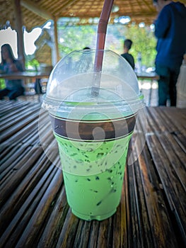 Iced milk green tea in plastic cup with lid and white straw on bamboo table in nature