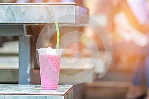 Iced milk pink tea in plastic cup  and green straw on marble chair