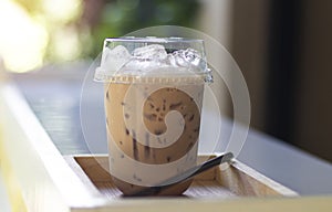 Iced milk tea in plastic glass, put on the wooden floor, behind it is a green garden