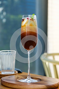Iced mix fruit juice with black cold brew coffee in wine glass on wooden table. Concept fusion drink menu summer drink