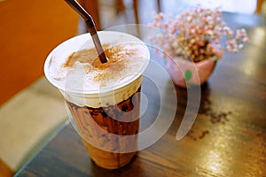 A iced mocha coffee with foamed milk topped with cinnamon powder placed on dark brown wooden table.