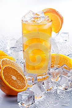 Iced orange juice in a glass with many condensation droplets, surrounded by ice cubes and slices of oranges