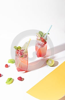 Iced red raspberry punch cocktail with lime in glass on color background. summer drink