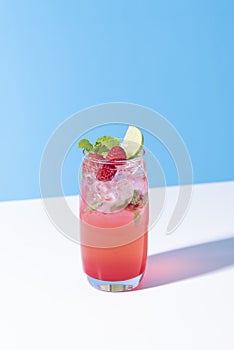 Iced red raspberry punch cocktail with lime in glass on color background. summer drink