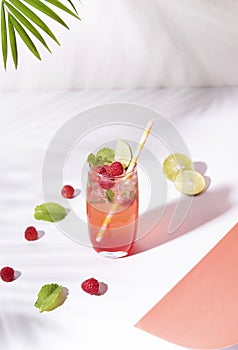 Iced red raspberry punch cocktail with lime in glass on color background. summer drink