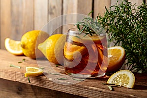 Iced tea or alcoholic cocktail with ice, rosemary and lemon slices on a old wooden table
