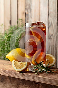 Iced tea or alcoholic cocktail with ice, rosemary and lemon slices on a old wooden table