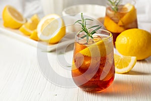 Iced tea or alcoholic cocktail with ice, rosemary and lemon slices on the white table
