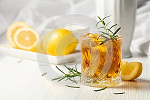 Iced tea or alcoholic cocktail with ice, rosemary and lemon slices on the white table