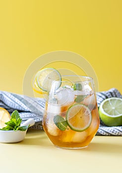 iced tea with ice, lemon, lime and mint in a glass on a yellow background