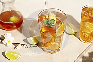 Iced tea with lemon, fresh mint leaves and ice in tall glasses with sun light and shadows