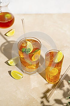 Iced tea with lemon, fresh mint leaves and ice in tall glasses with sun light and shadows