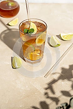 Iced tea with lemon, fresh mint leaves and ice in tall glasses with sun light and shadows