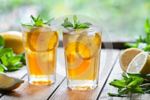 Iced tea with lemon slices and mint on wooden table with a view to the terrace and trees. Close up summer beverage