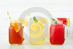 Iced tea, lemonade and watermelon juice summer drinks in mason jar glasses against white wood