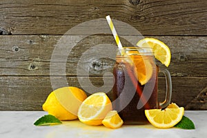 Iced tea in a mason jar glass with lemons, side view against dark wood