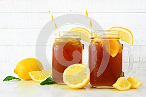 Iced tea in mason jar glasses with lemons, side view against white wood