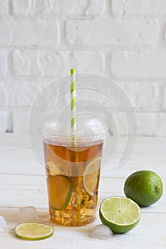 Iced tea in a plastic cup with straw with slice of lime. White w