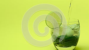 Iced tea in a transparent glass with mint with a slice of lime, an alcoholic drink pouring on a yellow background. Fresh drink