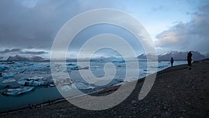 Woman takes picture at Jokulsatlon glacier lagoon close to diamond beach, icebergs float