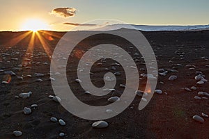 Iceland landscape black sand beach with stones and sunset flare