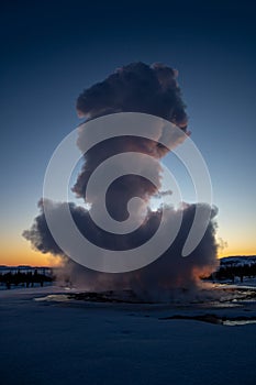 Iceland\'s great geyser Strokkur in full eruption with mist and smoke backlit and the last light of the orange sunset