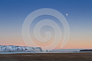 Iceland snowy mountain landscape near Vic village and beach, blue sky, crescent moon, empty space