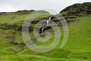 Icelandic landscape with green grass and hills full of waterfalls near the highway 1