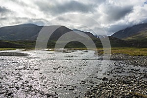 Icelandic landscape with river and mountains under cloudy sky in summer
