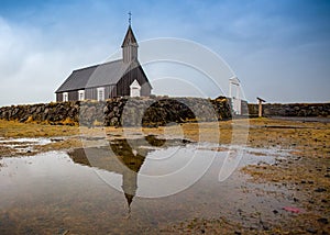 Icelandic style church with stone wall reflects in puddle