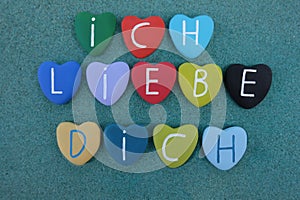 Ich Liebe Dich on multicolored stone hearts over green sand photo