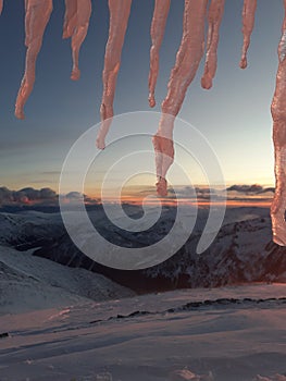 Icicles and dramatic sunset in the mountain. Cloudy sky at sunset. High mountain snowy landscape