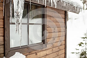 Icicles hang from the roof of a wooden house against a window in
