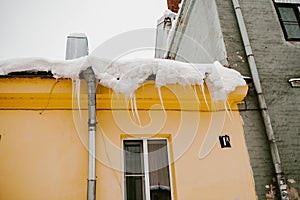 Icicles hang from the roof of a wooden house in the countryside, on a frosty cloudy day