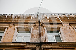 Icicles hang from the roof of a wooden house in the countryside, on a frosty cloudy day