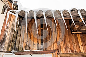 Icicles hang from the roof of a wooden house in the countryside, on a frosty cloudy day