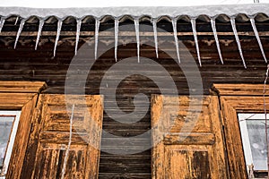 Icicles hang from the roof of a wooden house in the countryside, on a frosty cloudy day