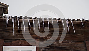 Icicles hang from the roof of a wooden house on a frosty, cloudy day