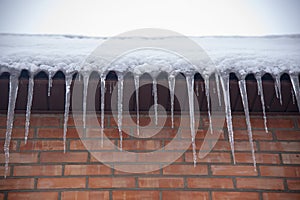 Icicles hanging from the roof against a brick wall .