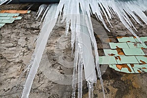 Icicles hanging from the roof of the old brick building with cubes of old tiles, traumatic acrid ice, thaw in the early spring, lo