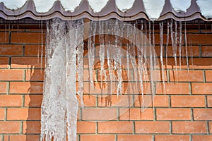 Icicles of ice hang from the edge of the roof against the red brick wall of the building. Background