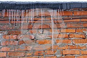 Icicles on the roof against a background of red brick brick wall