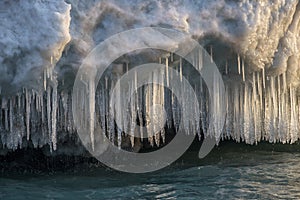 Icicles and snow dripping over water in sunlight