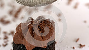 Icing sugar being sieved on chocolate cupcake